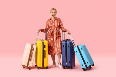 Pembe arka planda bavulları olan olgun bir kadın.