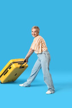 Mavi arka planda bavulu olan olgun bir kadın.