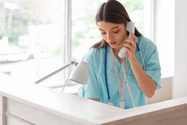 Klinikteki resepsiyonda telefonla konuşan kadın stajyer.