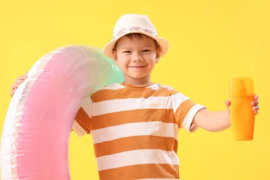 Güneş kremi şişesi ve sarı arka planda şişirilebilir yüzüğü olan küçük bir çocuk.