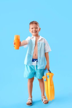 Güneş kremi şişesi ve mavi arka planda paletleri olan küçük bir çocuk.