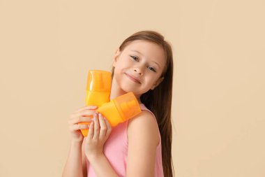 Bej arka planda güneş kremi şişeleri olan küçük bir kız.