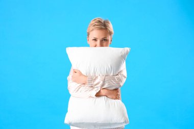 Mavi arka planda yastıklı pijamalı genç bir kadın.