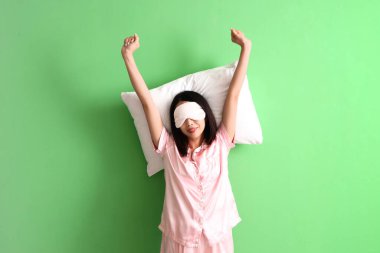 Yeşil arka planda yastıklı pijamalı güzel bir Asyalı kadın.