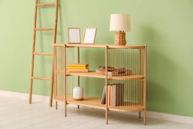 Boş çerçeveleri, lambaları, kitapları ve yeşil duvarın yanındaki merdivenleri olan şık ahşap raf ünitesi.