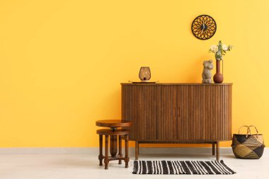 Süslü ahşap çekmeceler, sandalye, sepet ve saat turuncu duvarda asılı.