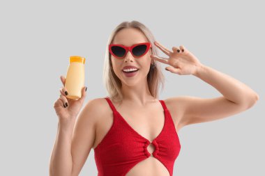 Güneş kremi sürmüş genç bir kadın arka planda zafer jesti gösteriyor.