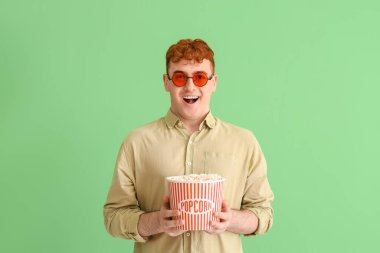 Yeşil arka planda patlamış mısırlı genç kızıl adam.