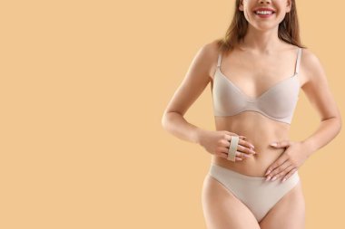 Bej arka planda anti-selülit fırçasıyla karnına masaj yapan genç bir kadın.