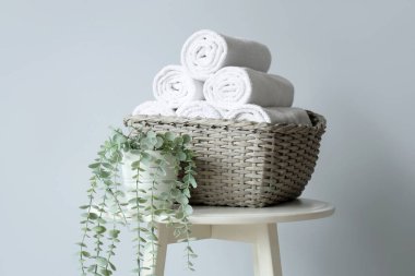 Havlularla dolu bir sepet ve ışık duvarının yanındaki masada bitki.