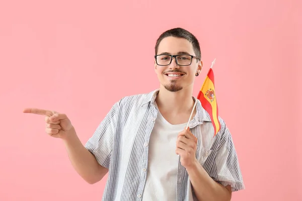Handsome young man with flag of Spain pointing at something on pink background