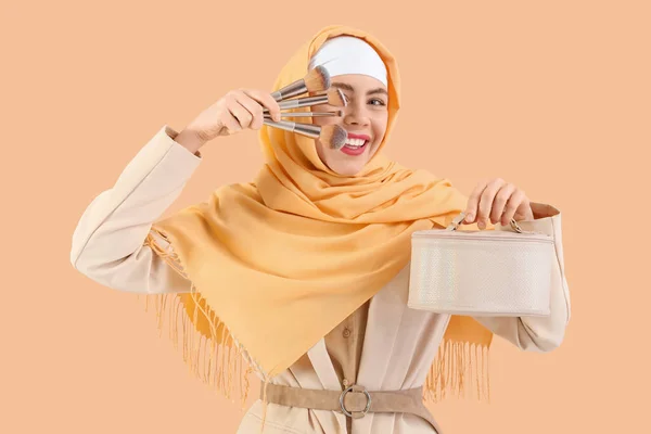 ベージュの背景に化粧バッグとメイクブラシが付いている美しいムスリム女性 — ストック写真