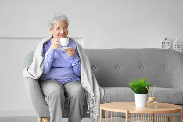 Senior woman with plaid drinking coffee on sofa at home
