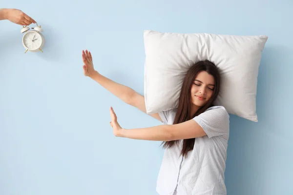 青い背景に目覚まし時計を拒否する枕を持つ不満の若い女性 — ストック写真
