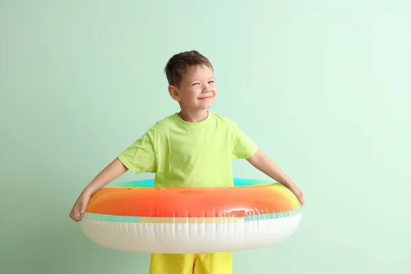 Little boy with inflatable ring and sunscreen cream on his face against pale green background