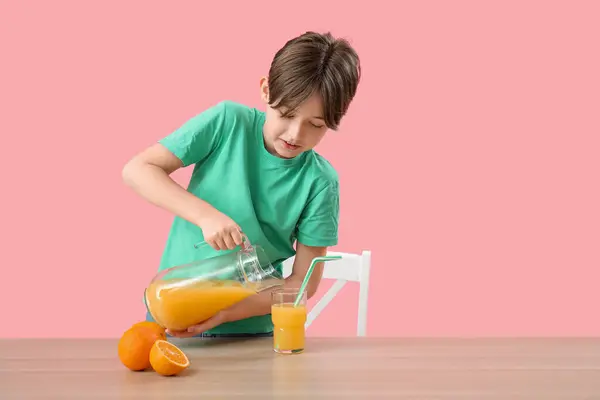 Mały Chłopiec Wylewa Sok Pomarańczowy Szkle Przy Stole Różowym Tle — Zdjęcie stockowe