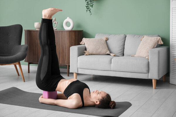 Sporty young woman practicing yoga with block at home