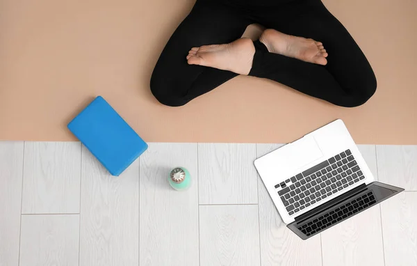 Woman with yoga block, bottle and laptop sitting on mat, top view