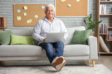 Evdeki kanepede dizüstü bilgisayar kullanan kıdemli adam.