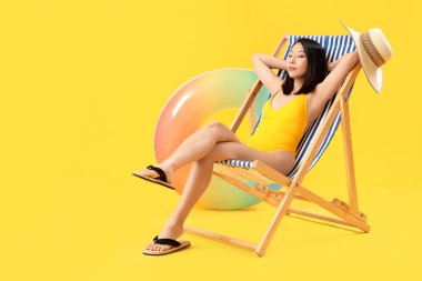 Güzel Asyalı kadın sarı arka planda iskemlede dinleniyor.