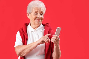 Kırmızı arka planda cep telefonu kullanan son sınıf öğrencisi.