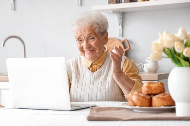 Üst düzey kadın mutfaktaki masada dizüstü bilgisayar kullanıyor.