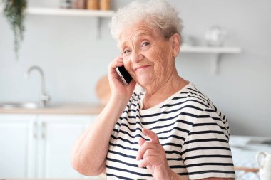 Üst düzey kadın mutfakta cep telefonuyla konuşuyor, yakın plan.