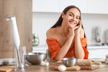 Yüzünde un olan genç bir kadın mutfakta hamur hazırlıyor.