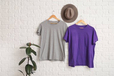 Beyaz duvarda asılı şık tişörtler ve şapkalar