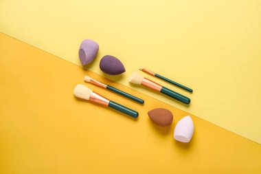 Sarı arka planda makyaj süngerleri ve fırçalar