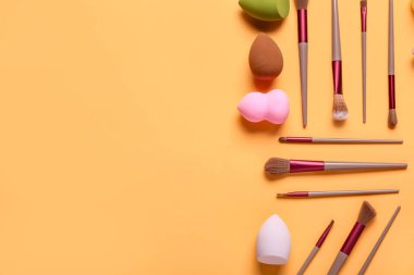Turuncu arka planda makyaj süngerleri ve fırçalar