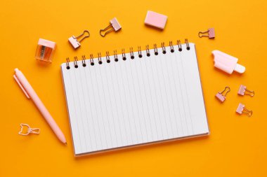 Turuncu arka planda farklı kırtasiye malzemesi içeren defter