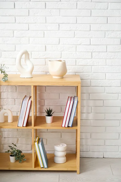 Bookshelf with houseplants near white brick wall in room