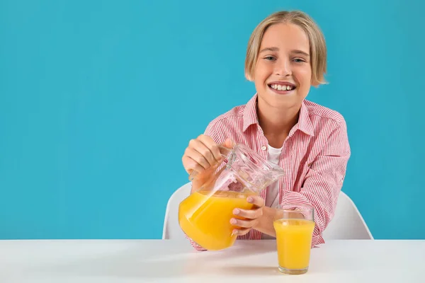 Little boy pouring orange juice into glass at table on blue background