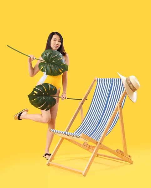 Schöne Asiatin Mit Palmblättern Und Liegestuhl Auf Gelbem Hintergrund — Stockfoto