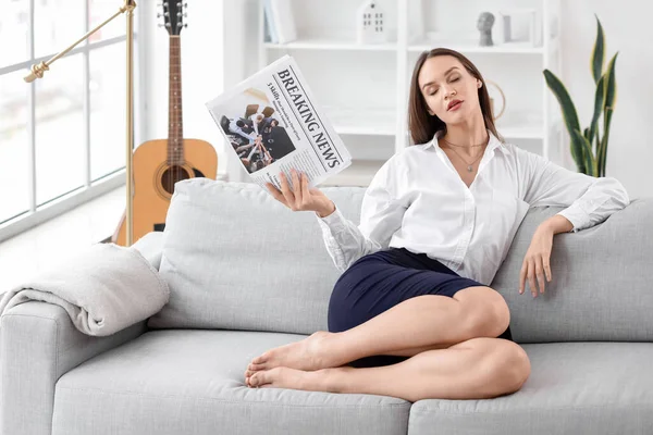 Young businesswoman with newspaper resting at home after long working day