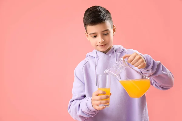 Mały Chłopiec Wlewający Sok Pomarańczowy Szklanki Różowym Tle — Zdjęcie stockowe