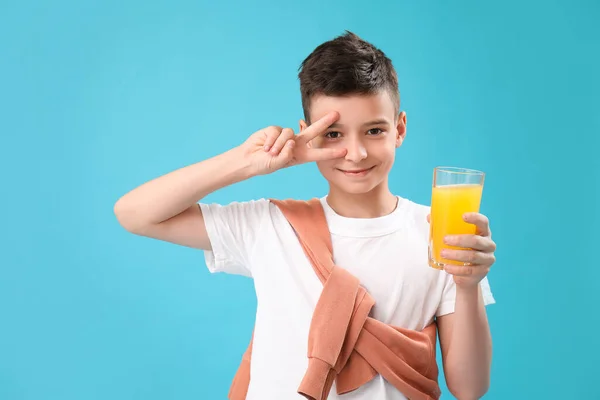 Mały Chłopiec Szklanką Soku Pomarańczowego Pokazując Gest Zwycięstwa Niebieskim Tle — Zdjęcie stockowe
