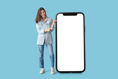 Modaya uygun kot elbiseli ve açık mavi arka planda büyük cep telefonlu genç bir kadın. Tasarım için pankart