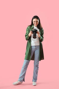 Pembe arka planda profesyonel kamerası olan kadın fotoğrafçı.