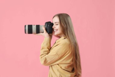 Pembe arka planda profesyonel kameralı genç bayan fotoğrafçı.