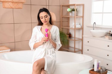 Banyoda pembe vibratörlü genç bir kadın var.