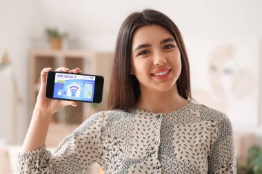 Akıllı ev güvenlik kontrol paneli olan cep telefonu tutan genç bir kadın.