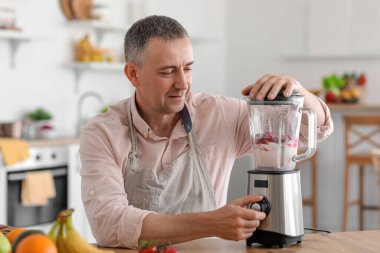 Olgun adam mutfakta blender ile meyve suyu yapıyor.