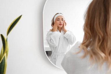 Banyoda aynanın yanında yüz geliştirme egzersizi yapan genç bir kadın.