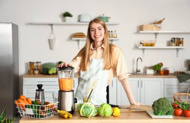 Genç bir kadın mutfakta blender ile sağlıklı smoothie yapıyor.