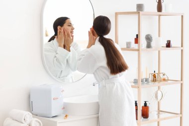 Banyoda aynanın yanında yüz geliştirme egzersizi yapan genç bir kadın.