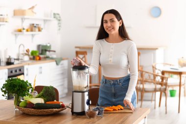 Genç bir kadın mutfakta blender ile sağlıklı smoothie yapıyor.