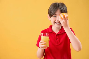Arka planda portakal suyu ve bir bardak meyve suyu olan küçük bir çocuk.