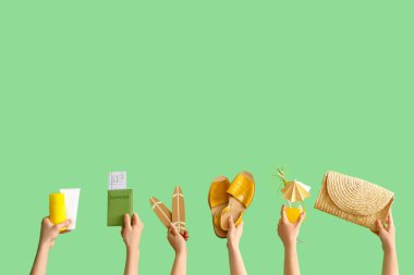 Yeşil arka planda plaj aksesuarları, pasaport ve kokteyli olan birçok el.